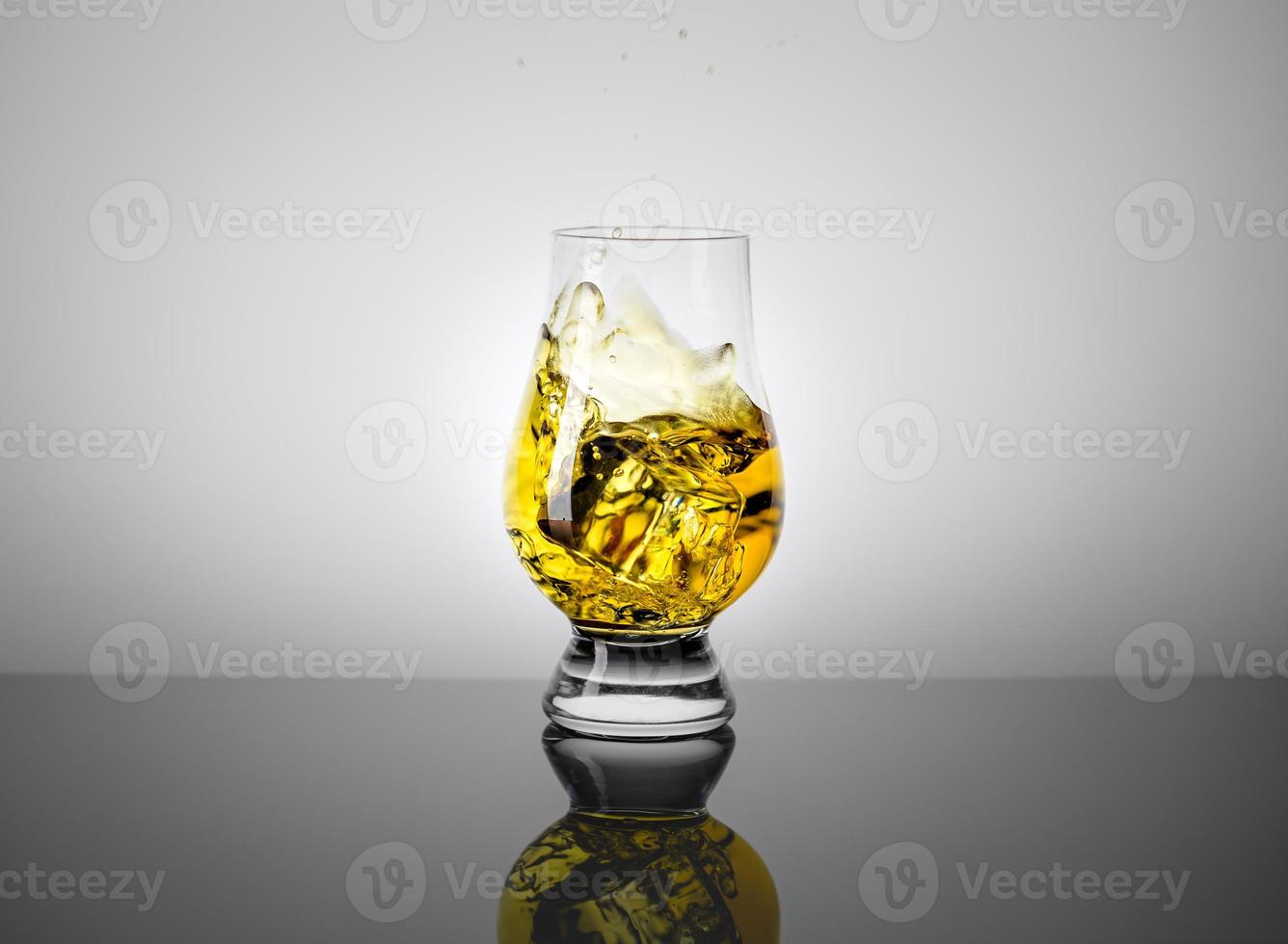 vaso de prueba con un trago de whisky escocés y cubitos de hielo cayendo en él. foto