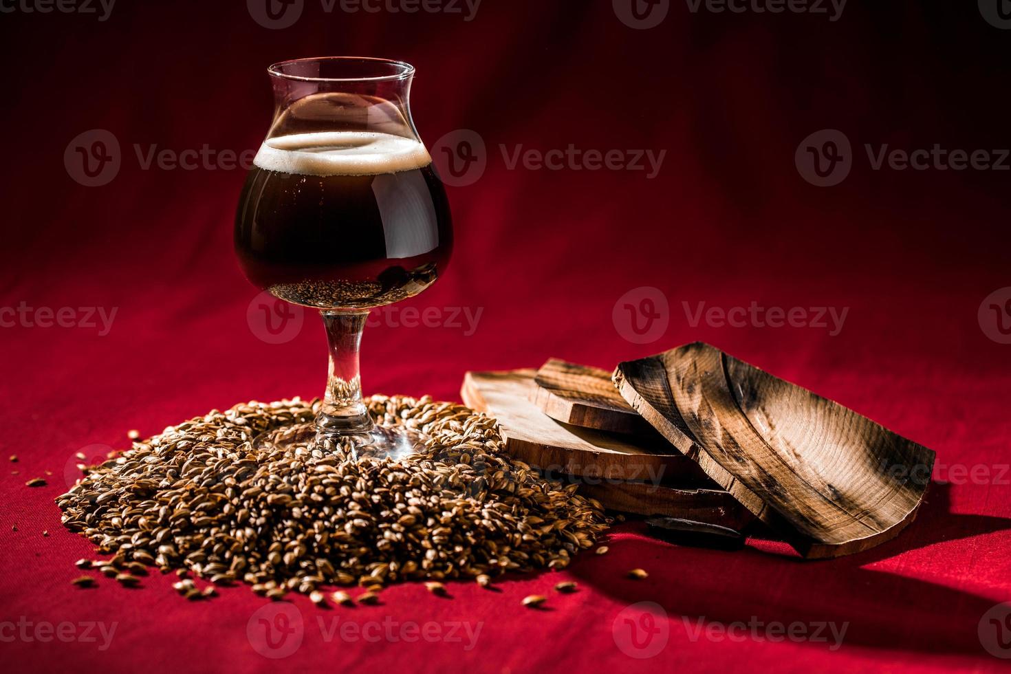 Barril de cerveza oscura envejecida sobre un montón de grano malteado, madera y fondo rojo. foto