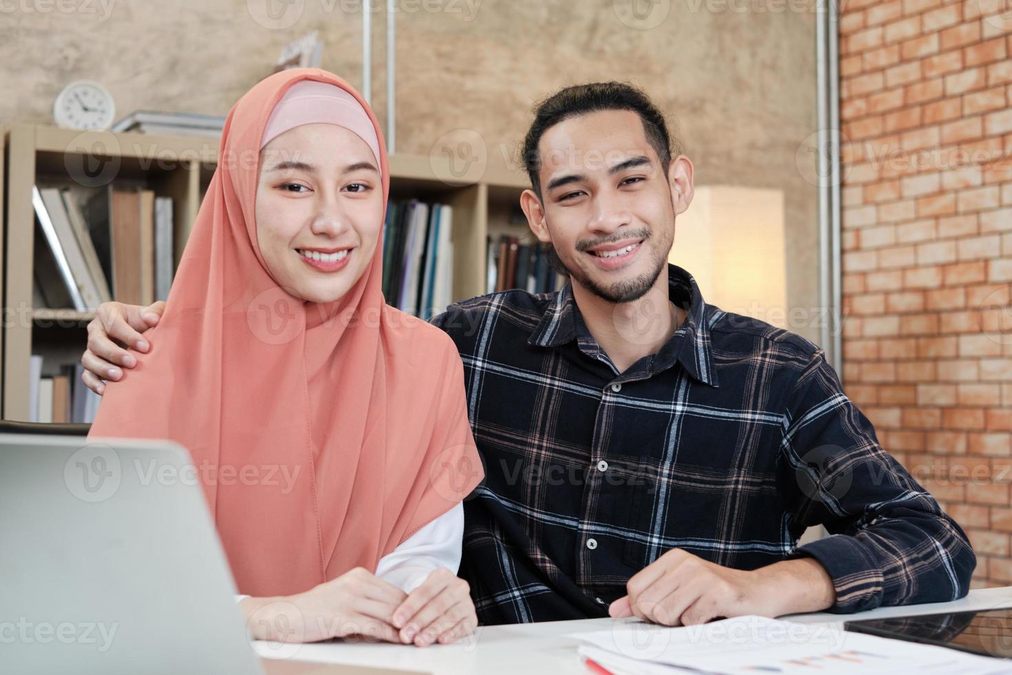 retrato de personas emprendedoras de inicio de negocios, hombre joven y hermosa mujer propietaria, dos socios que pareja islámica, mirando a la cámara, sonríe felizmente en la pequeña oficina de trabajo de comercio electrónico. foto