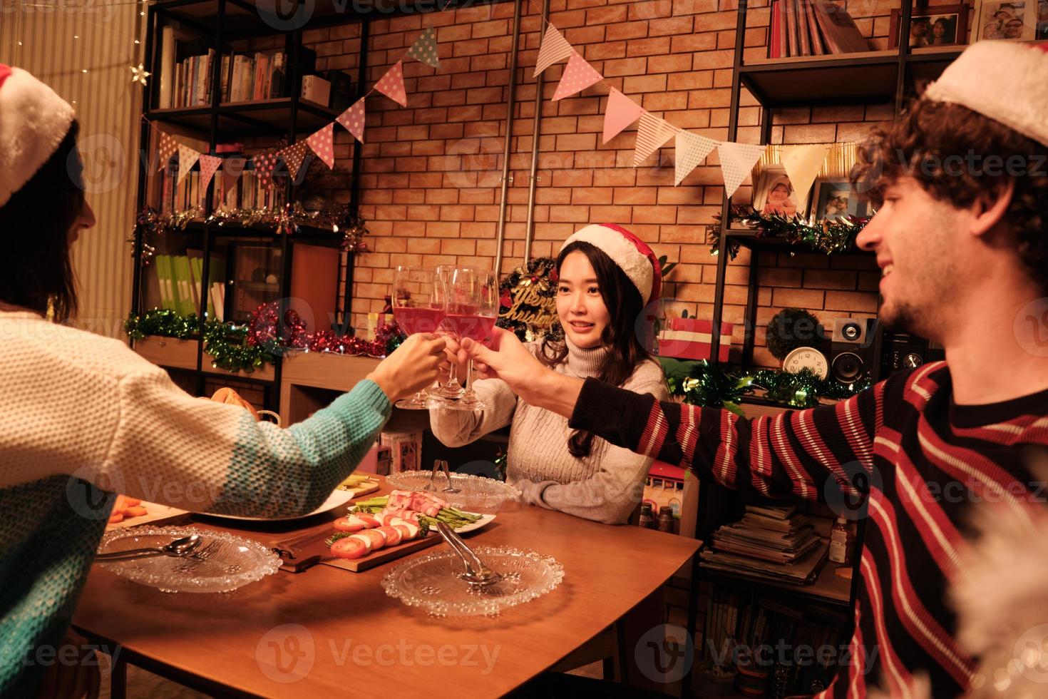 Happiness family and friends are celebrating, raising glasses and a cheerful smile with drinks, enjoy eating foods in home's dining room, decorated for Christmas festival party and New Year's Day. photo
