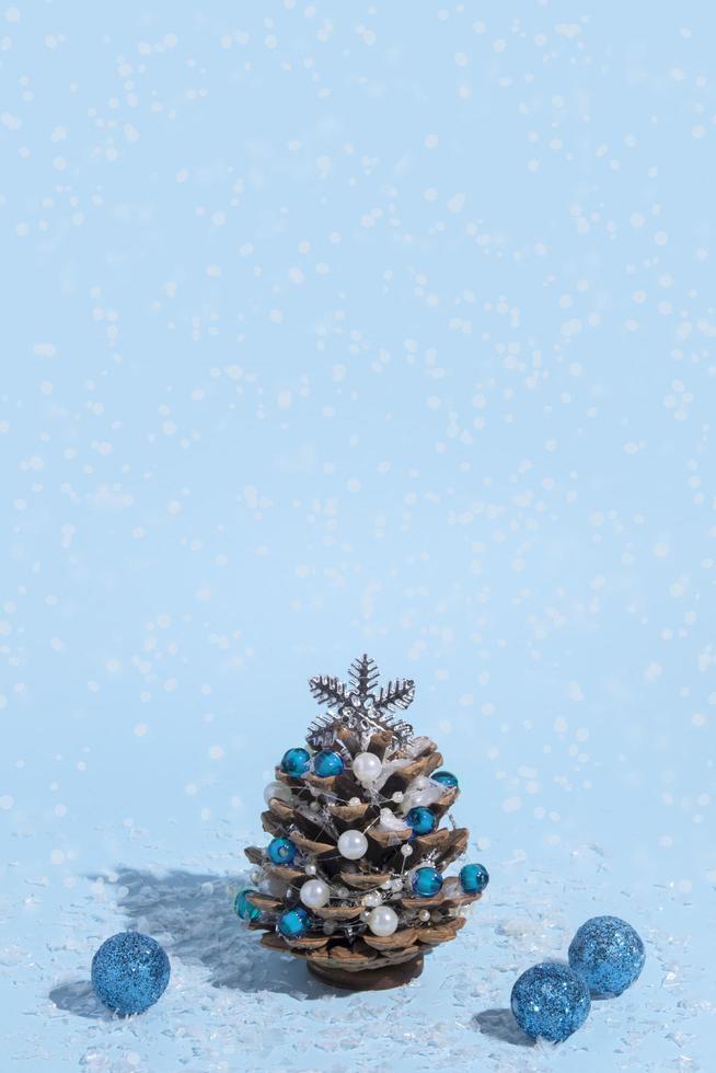 Árbol de Navidad alternativo hecho de piñas con perlas y nieve sobre un fondo azul con una sombra dura foto