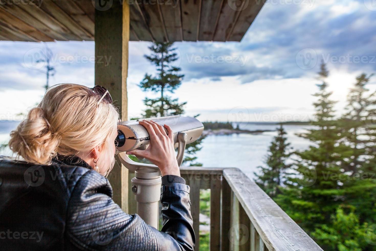 Young Woman Looking at the Amazing Nature Through a Binocular in a Observation Tower photo