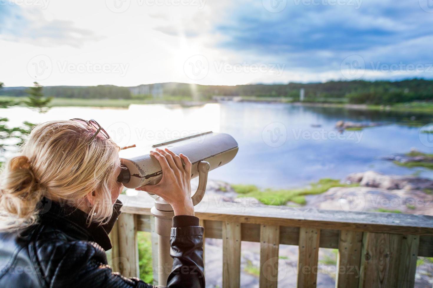 Mujer joven mirando la naturaleza asombrosa a través de un binocular en una torre de observación foto