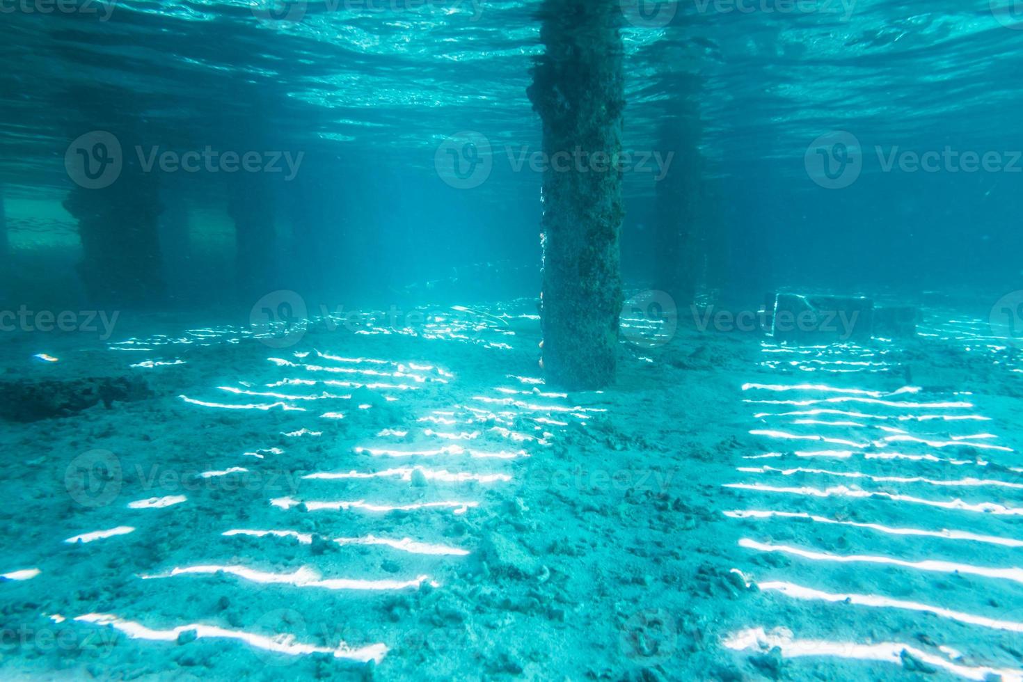 Vista submarina de debajo de un muelle con pilares y luz solar foto