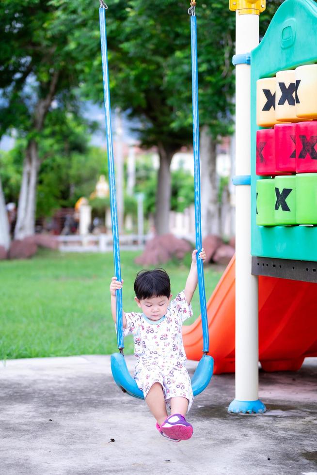 Little boy was sitting on swing. Legs float on the floor. Lightly swing. Toddler kid  aged 2 year old. Handsome child loves blue swings. Children play in playground. photo