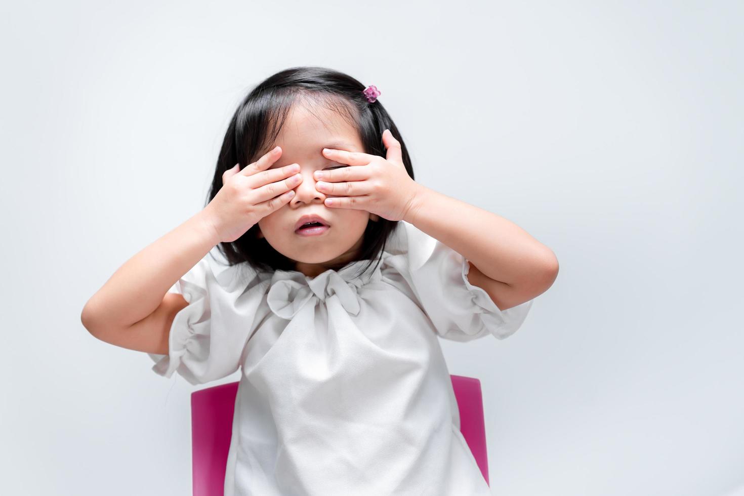 Adorable kid covering her eyes with hands over white background. Child playing hide and seek. photo