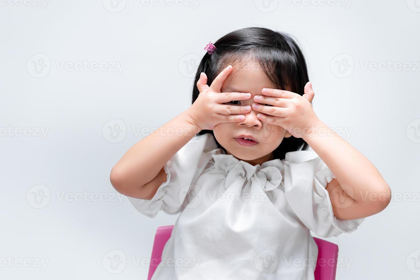 Niña de 4 años sobre las manos en los ojos. niño jugando al escondite. sobre fondo blanco aislado. foto