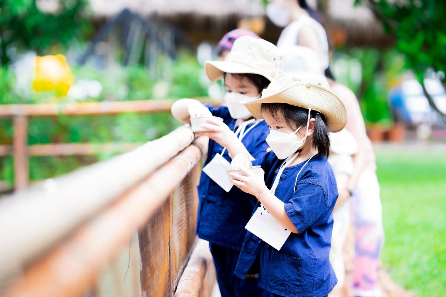 Two sisters are having fun in the simulation of farm life. Children are tasked with caring for the fish in the pond. Kids feeding food to fish. photo