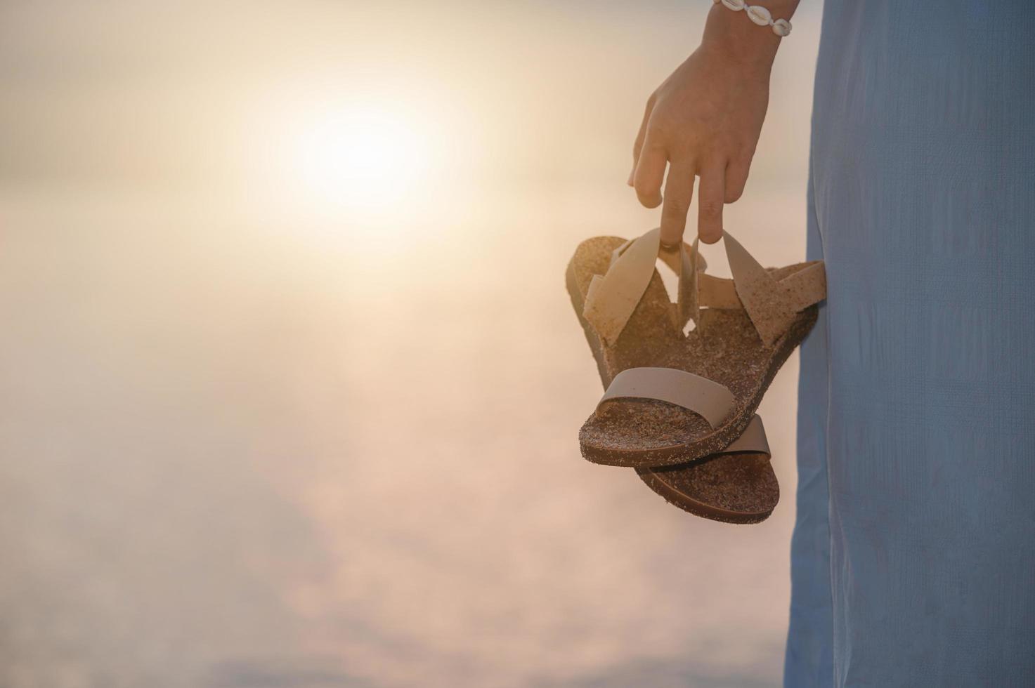 Mujer sosteniendo sandalias caminando por la playa foto