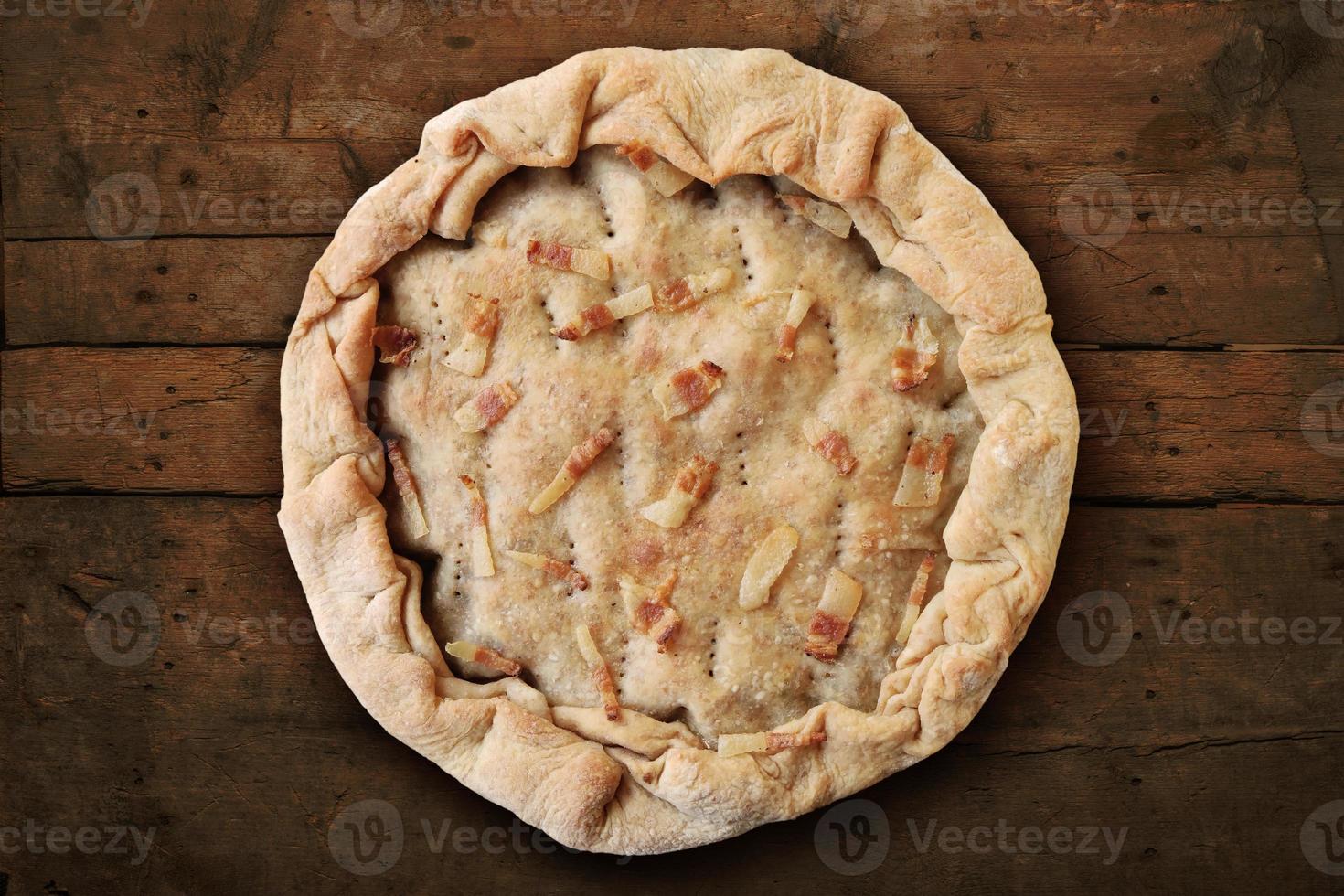 Whole salted pie with bacon on rough wooden table photo