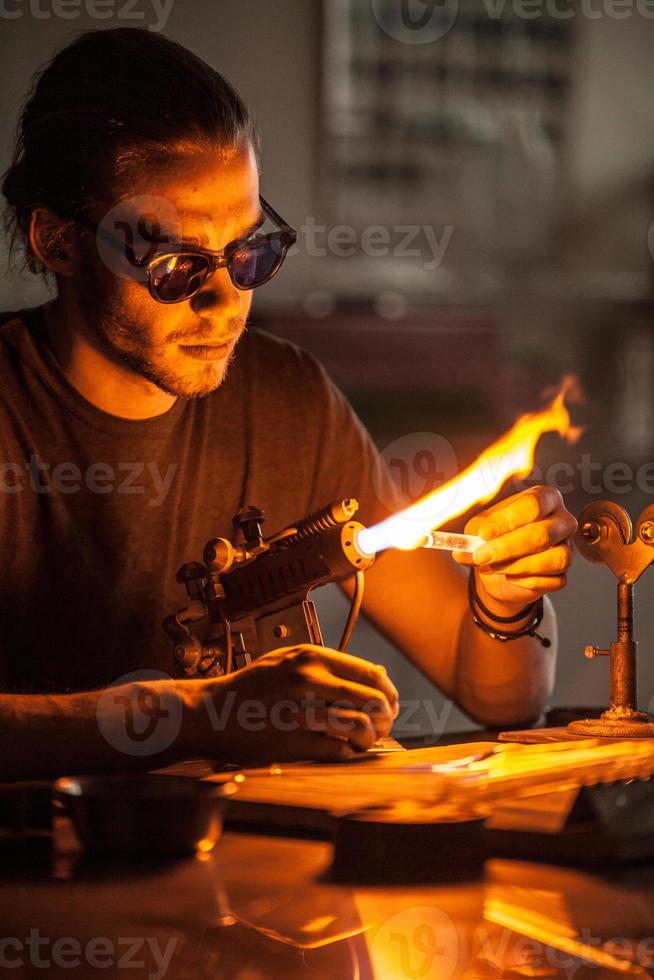 soplado de vidrio joven trabajando en una llama de antorcha con tubos de vidrio foto