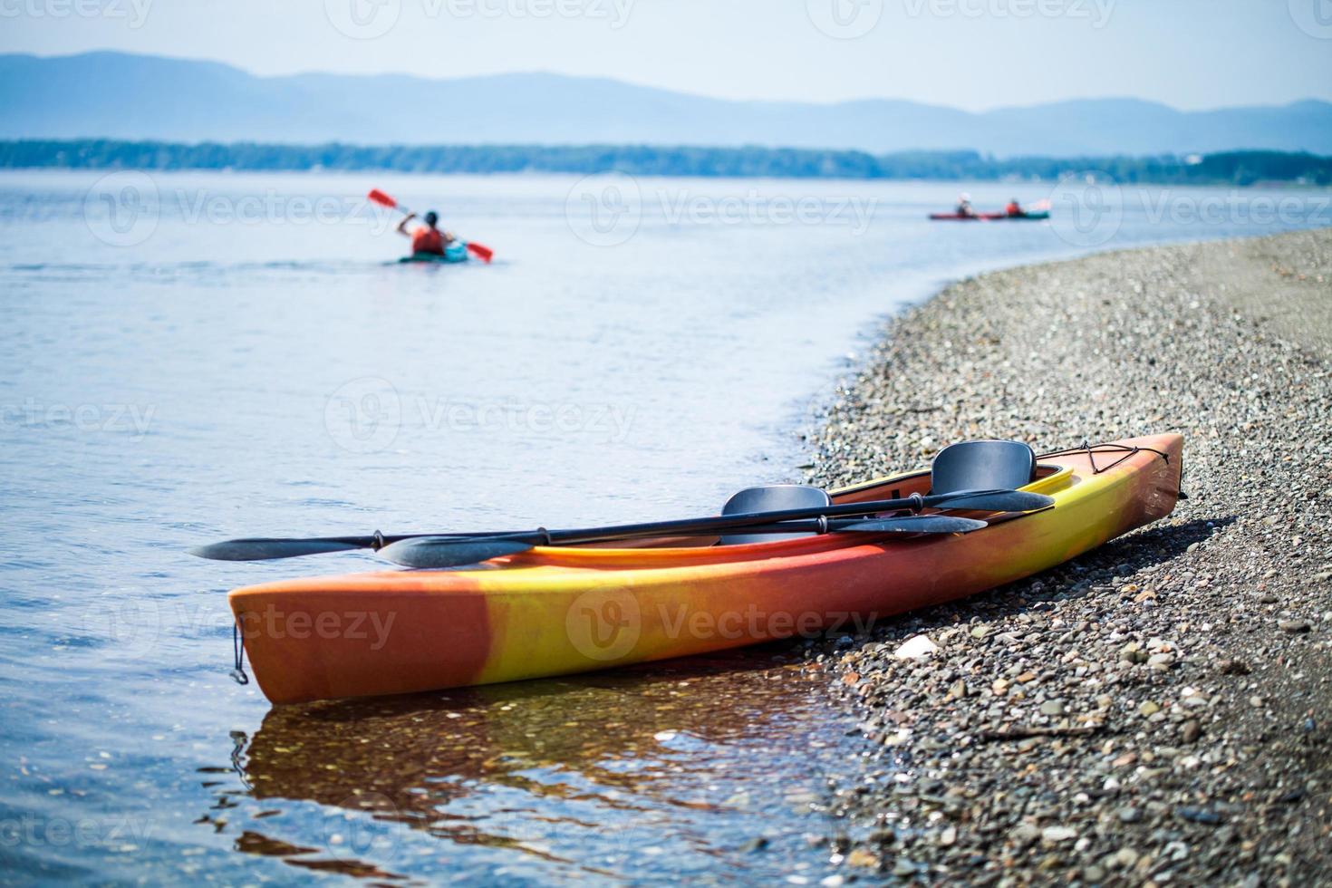 Kayak en la orilla del mar con kayakistas en el fondo foto