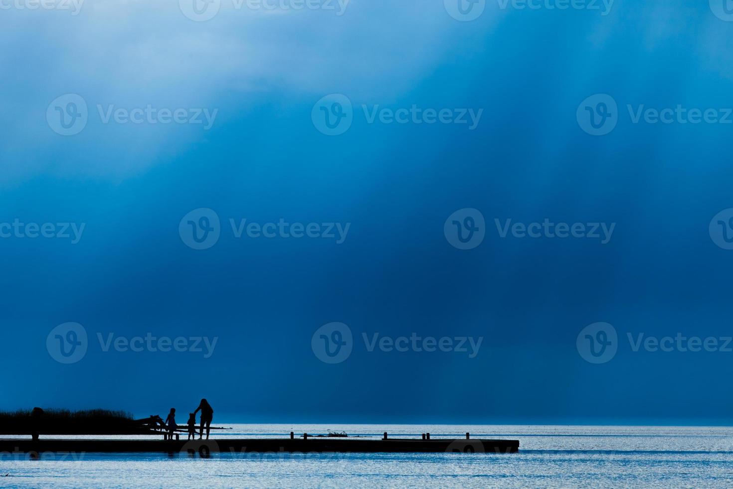 Dock in silhouette with people and rays of light photo