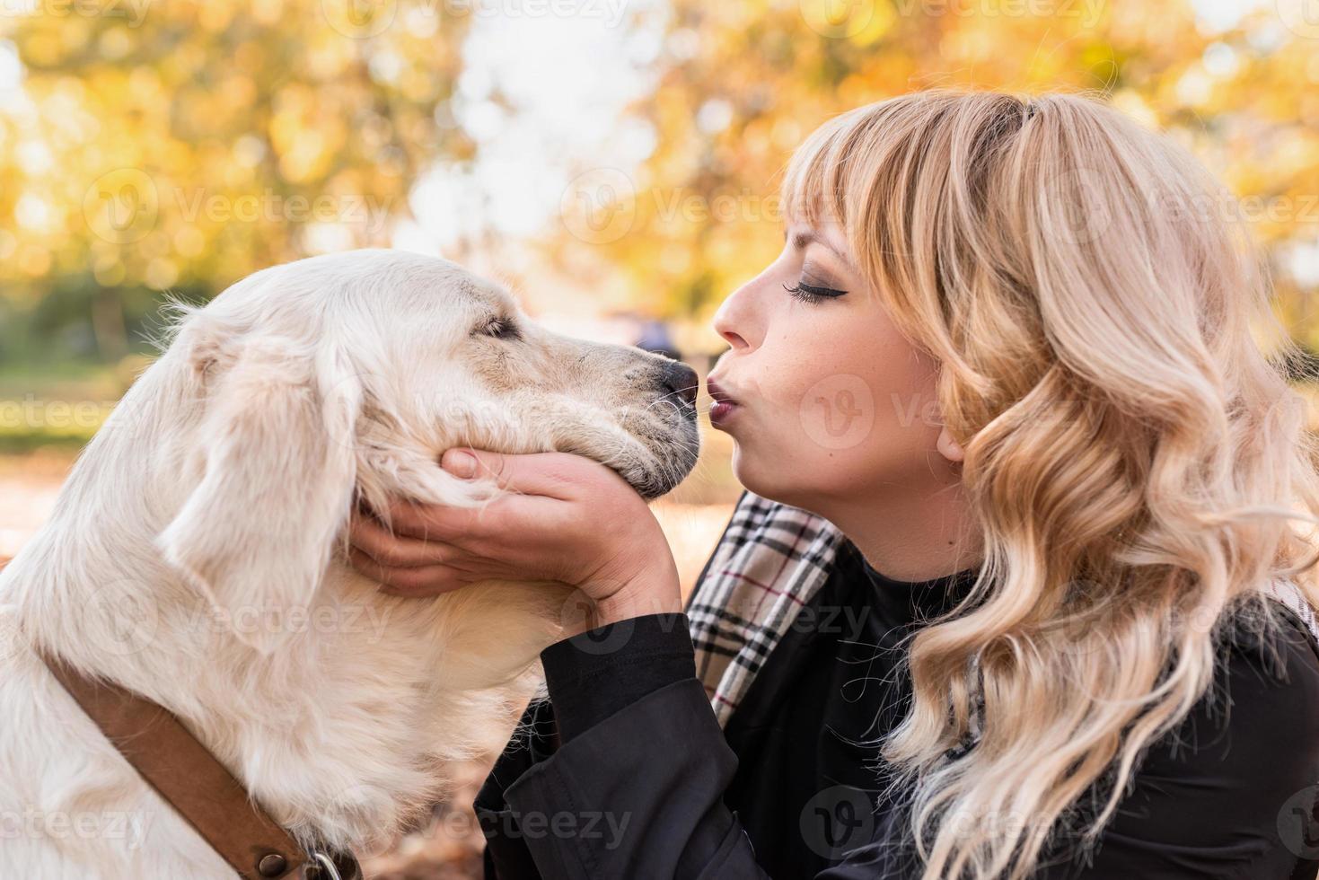 Feliz mujer propietaria besando a su perro retriever en el parque de otoño foto