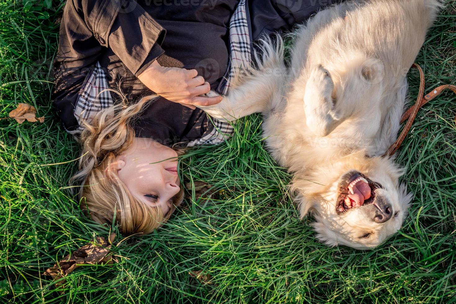 Beautiful caucasian woman laying in the grass with her golden labrador retriever dog at a park in the sunset photo