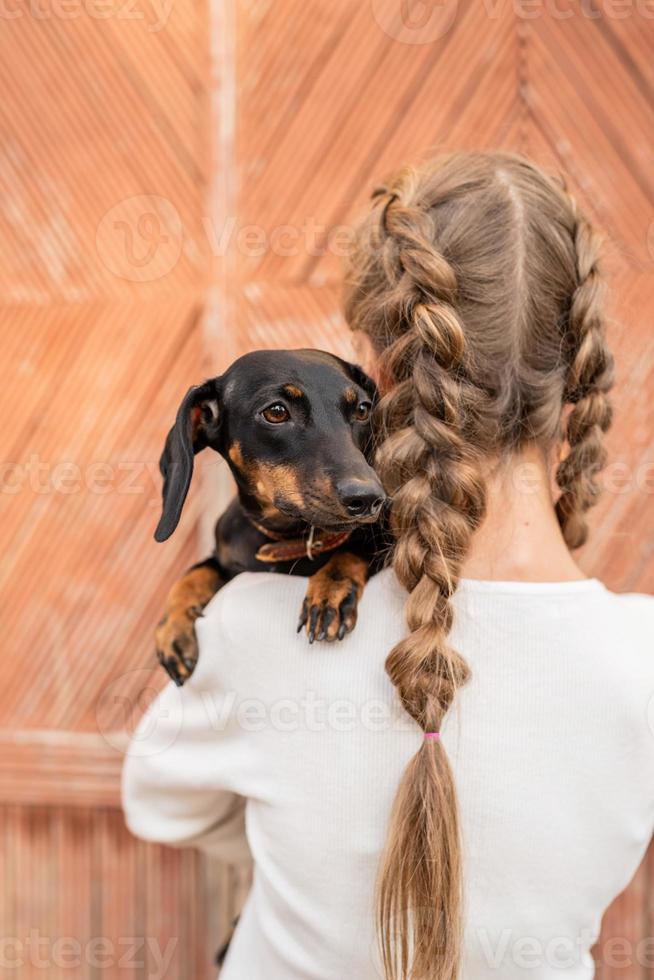 Mujer joven con cabello trenzado sosteniendo su mascota teckel en sus brazos al aire libre foto