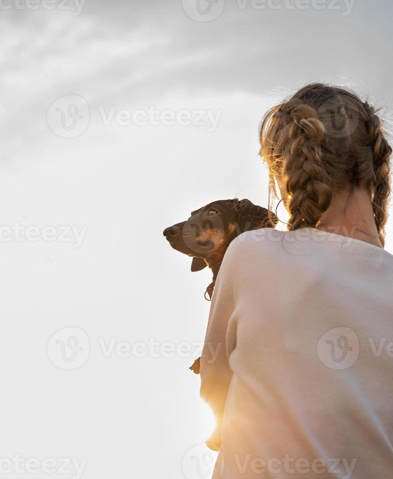 teenager girl holding her dachshund dog in her arms outdoors in sunset photo