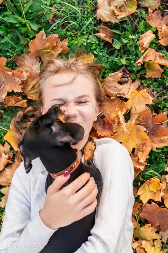 Mujer joven jugando con su perro teckel tendido en el césped foto