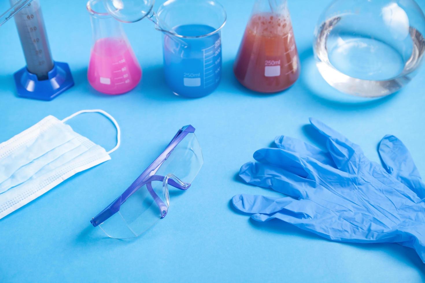 cristalería científica con guantes y vasos líquidos de colores. foto