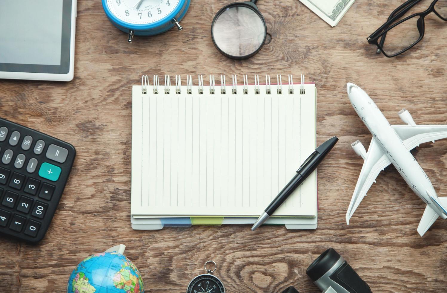 Notepad with pen and travel items on the wooden background. photo