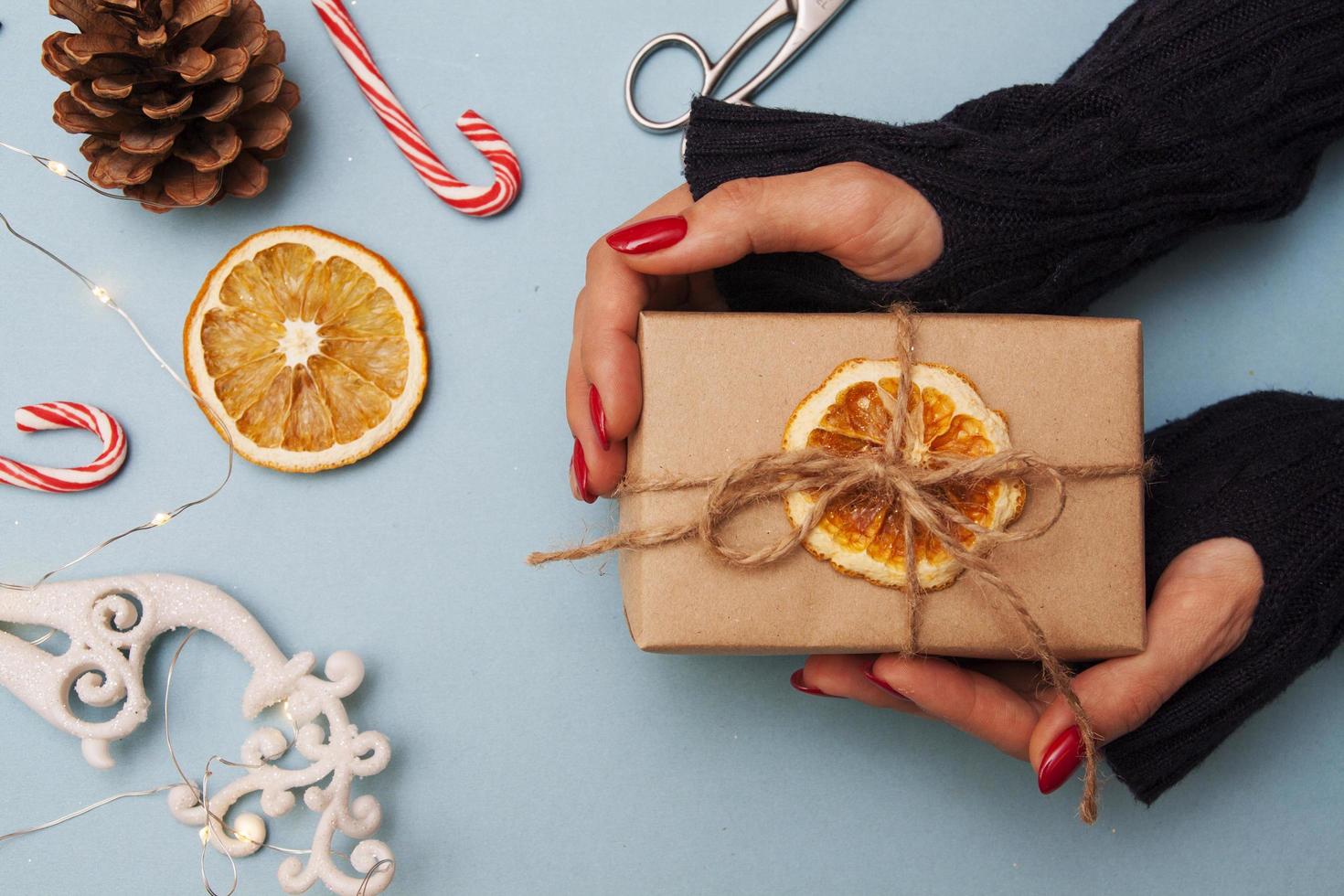 New Year flat lay with a gift in hand. A girl in a sweater holds a box with a bow in her hands on the background of Christmas decor. photo