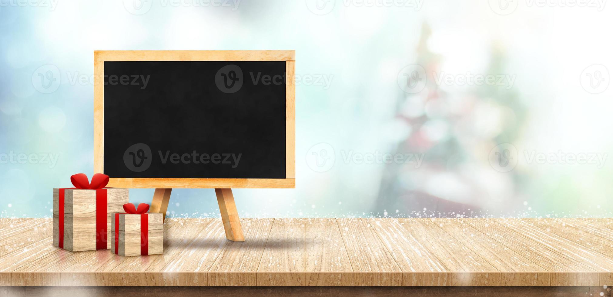 Blank blackboard with gift box on wood table top with christmas tree blurred photo