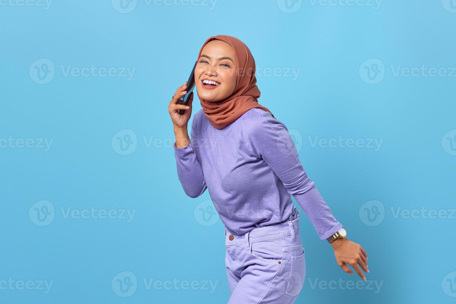 Alegre joven asiática hablando por un teléfono móvil con su novio aislado sobre fondo azul. foto