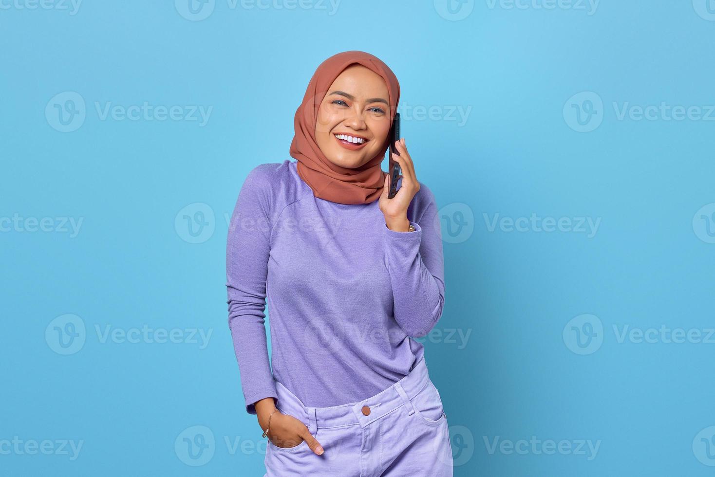 Smiling young Asian woman talking on a mobile phone with her boyfriend isolated on blue background photo