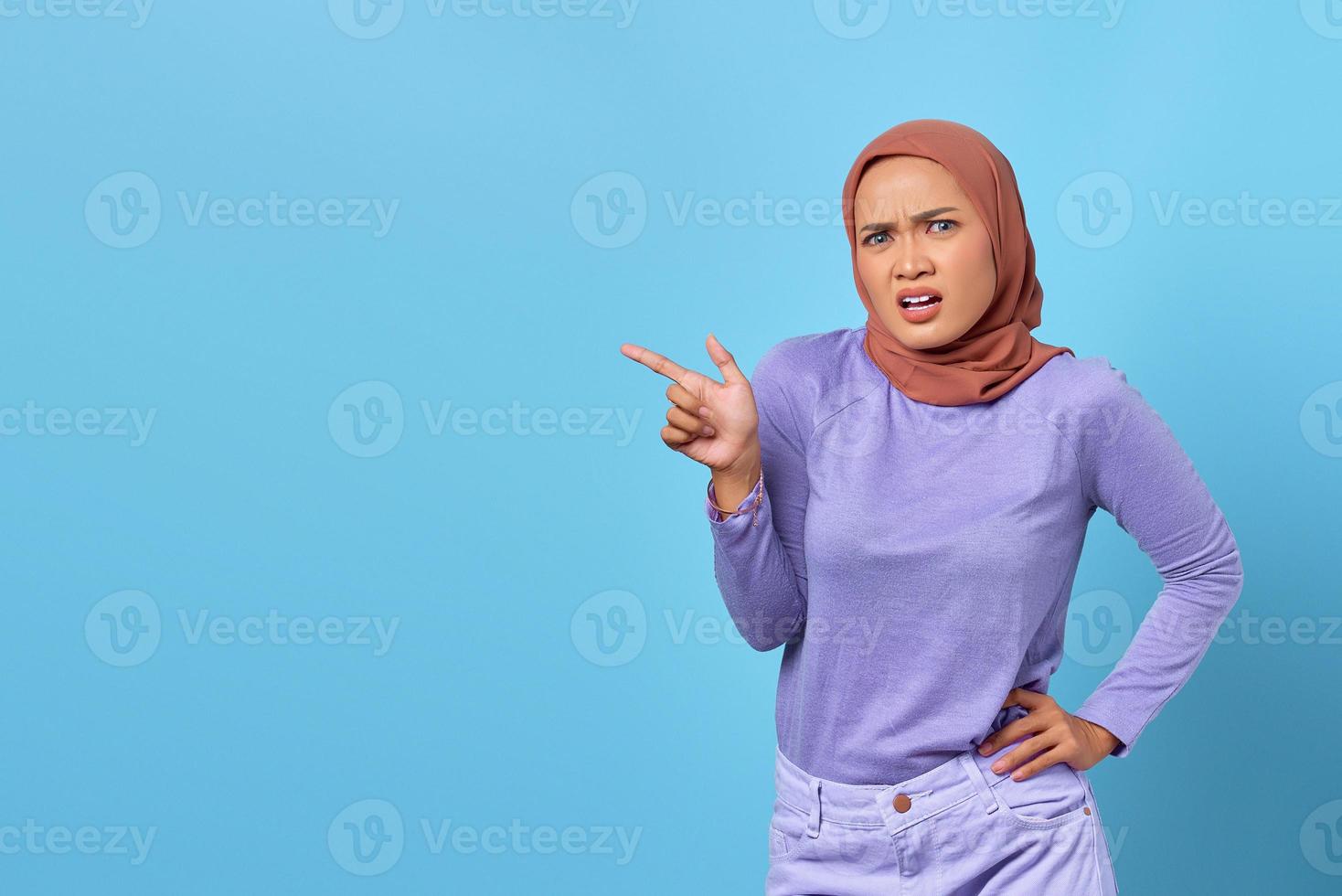 Portrait of shocked young Asian woman pointing finger at copy space on blue background photo