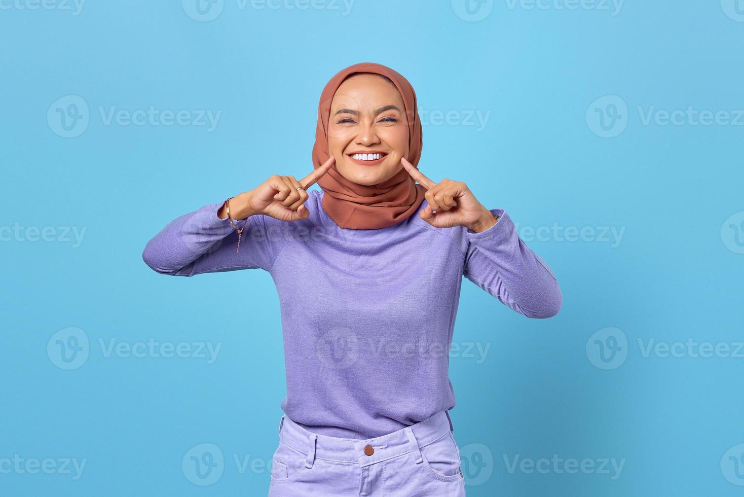 retrato, de, atractivo, joven, mujer asiática, señalar, en, dientes blancos, sano, en, fondo azul foto