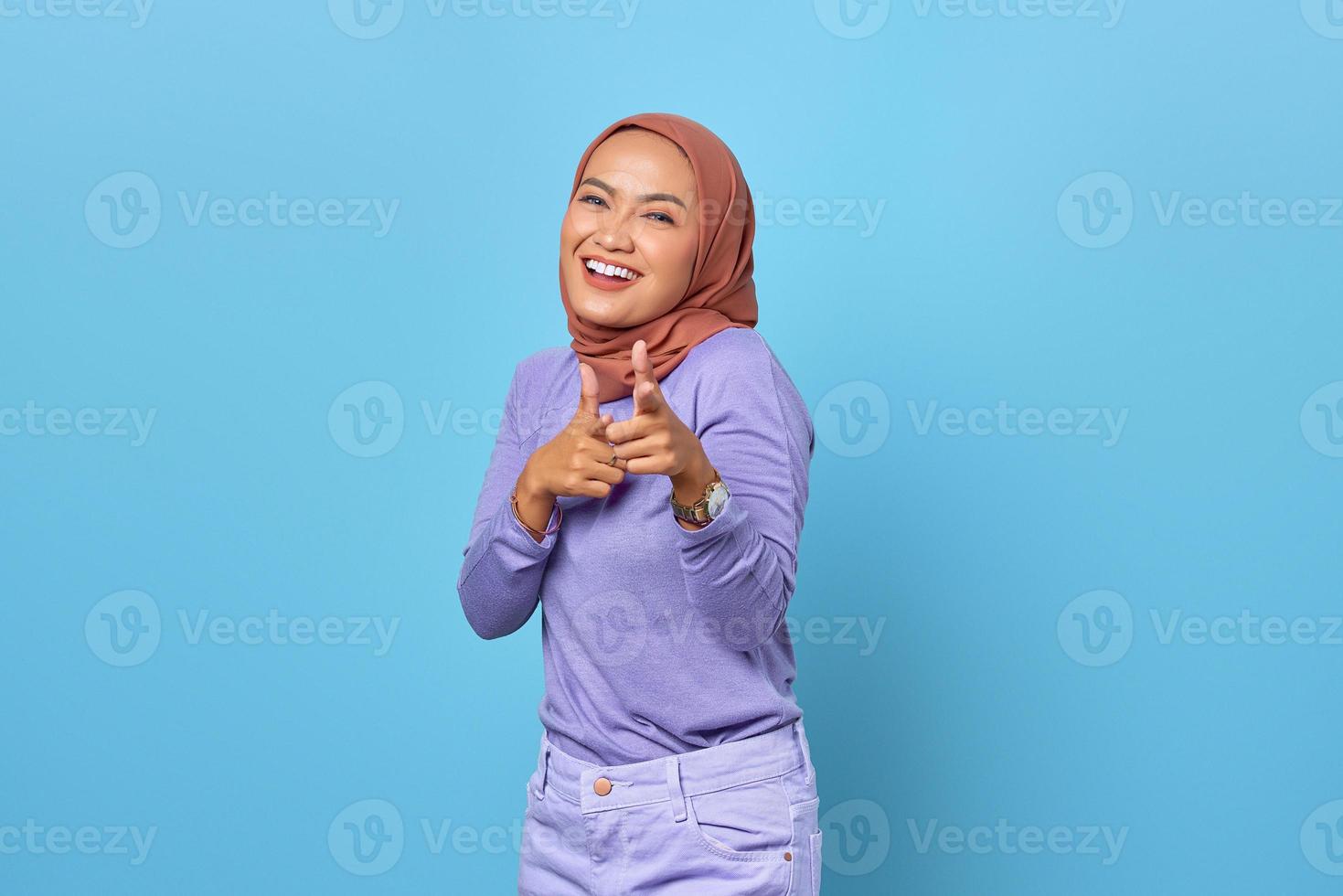 Retrato de joven alegre mujer asiática apuntando con el dedo a la cámara sobre fondo azul. foto