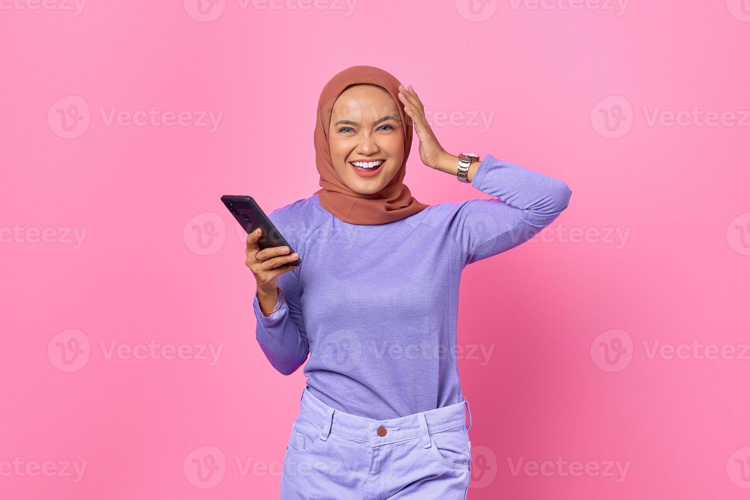 Portrait of smiling young Asian woman holding mobile phone on pink background photo