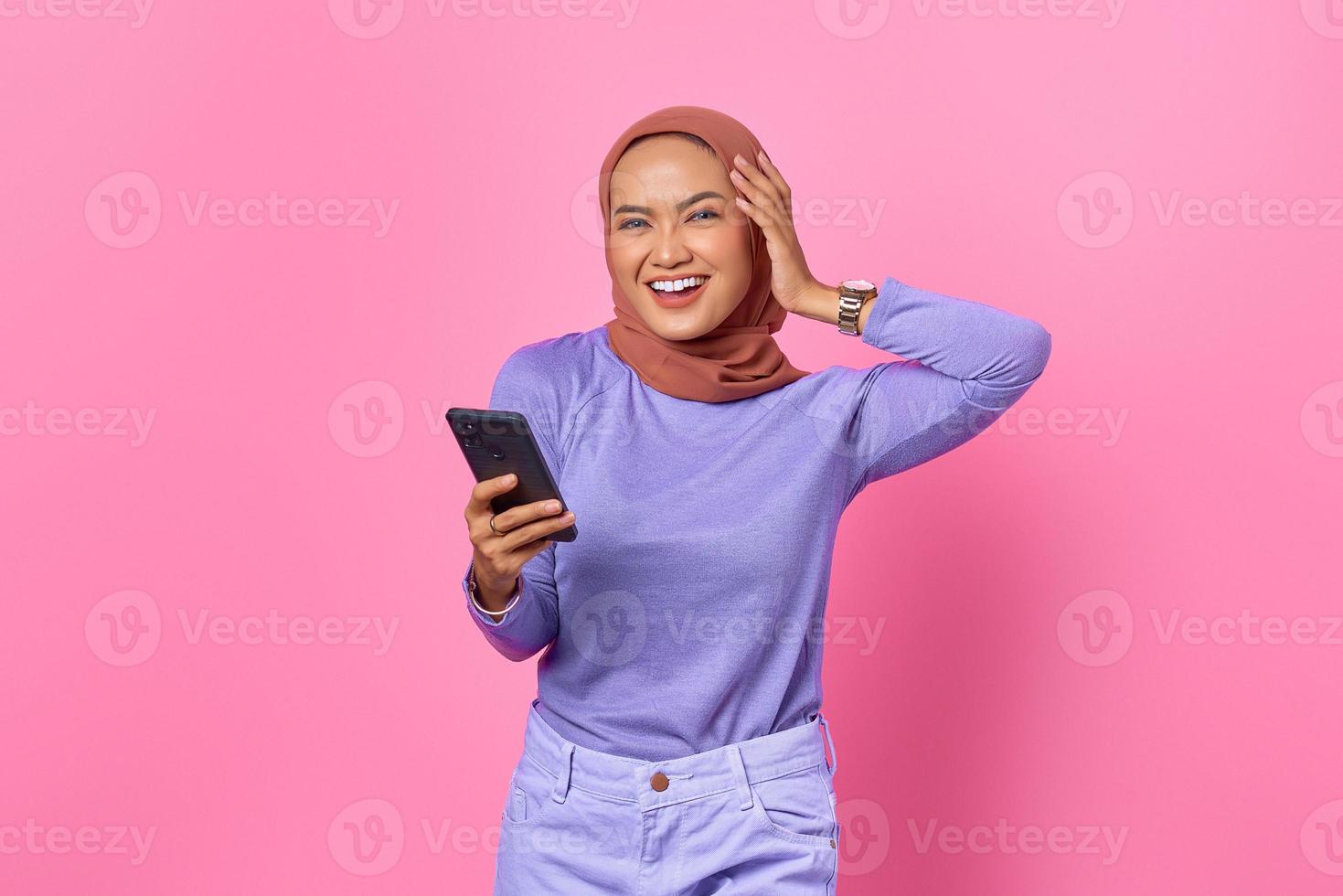 retrato, de, sonriente, joven, mujer asiática, tenencia, teléfono móvil, en, fondo rosa foto