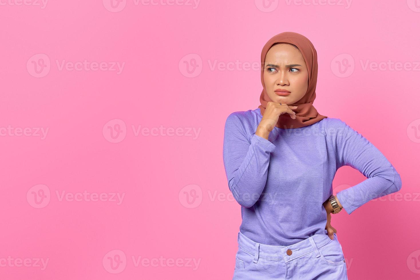 Retrato de mujer asiática joven pensativa tocando la barbilla con la mano y mirando a un lado sobre fondo de color rosa foto