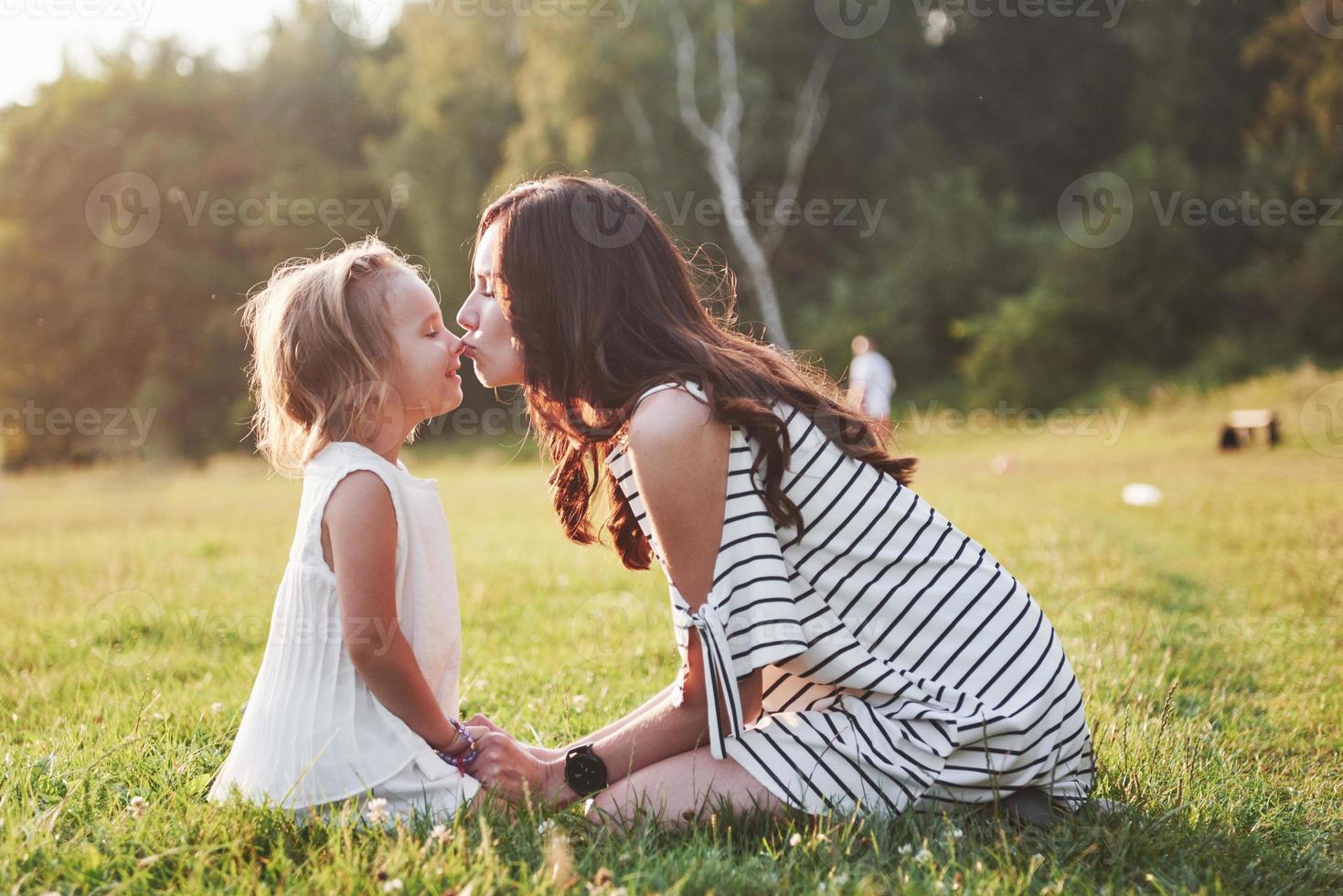 feliz madre e hija abrazándose en un parque bajo el sol sobre un fondo de verano brillante de hierbas. foto