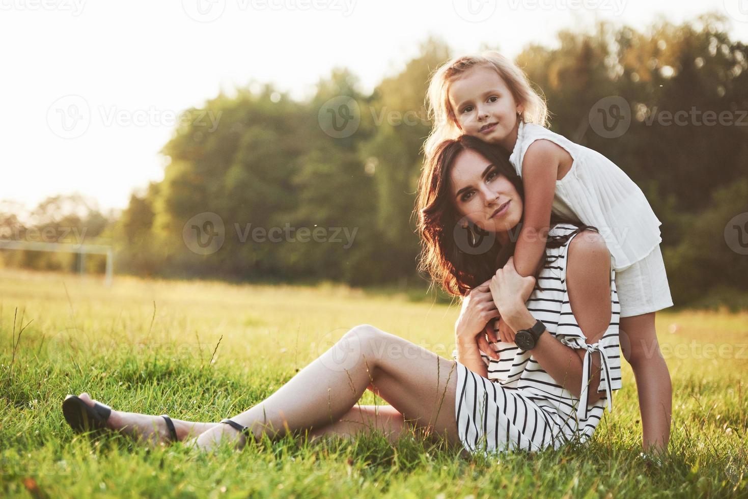 feliz madre e hija abrazándose en un parque bajo el sol sobre un fondo de verano brillante de hierbas. foto