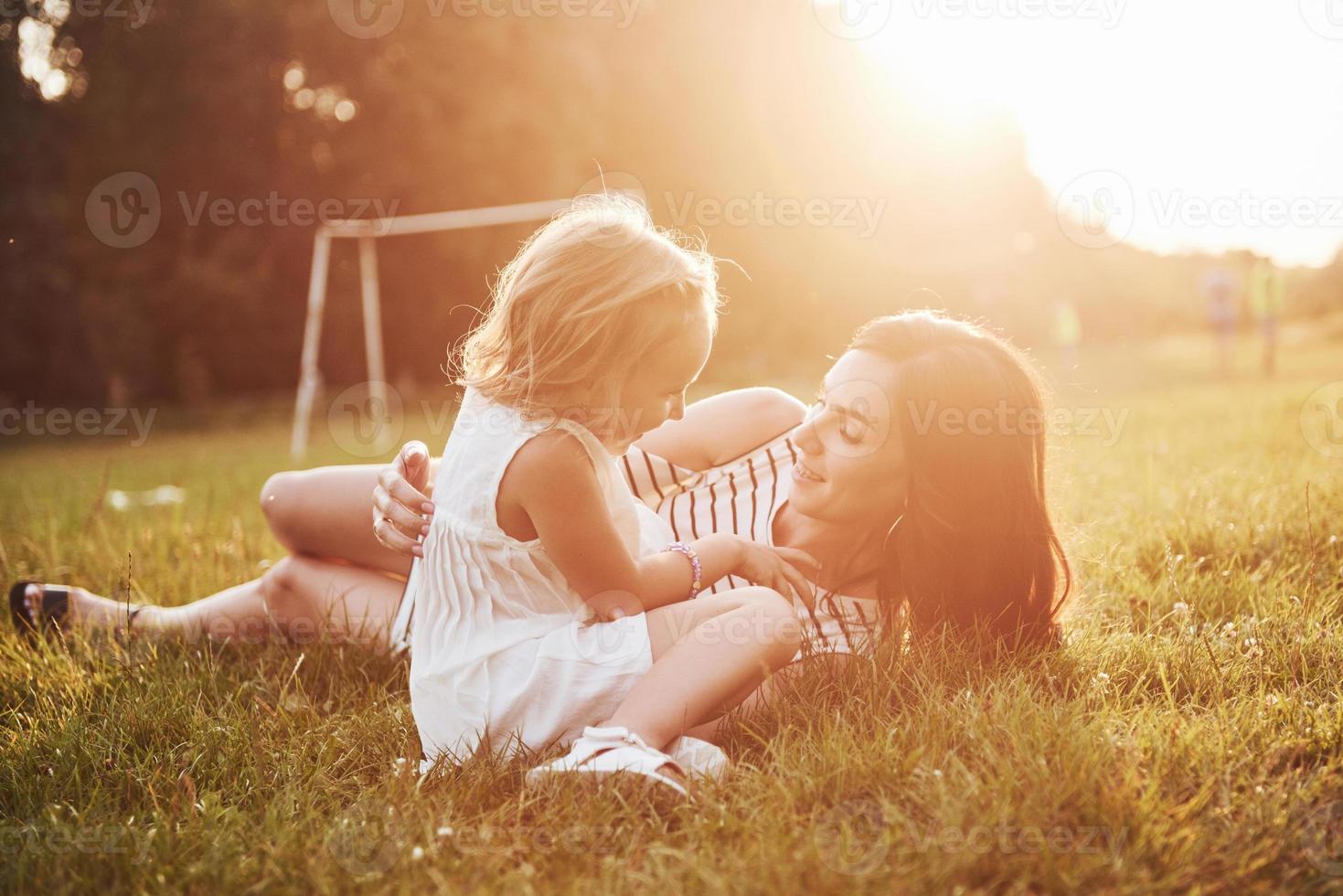 feliz madre e hija abrazándose en un parque bajo el sol sobre un fondo de verano brillante de hierbas. foto