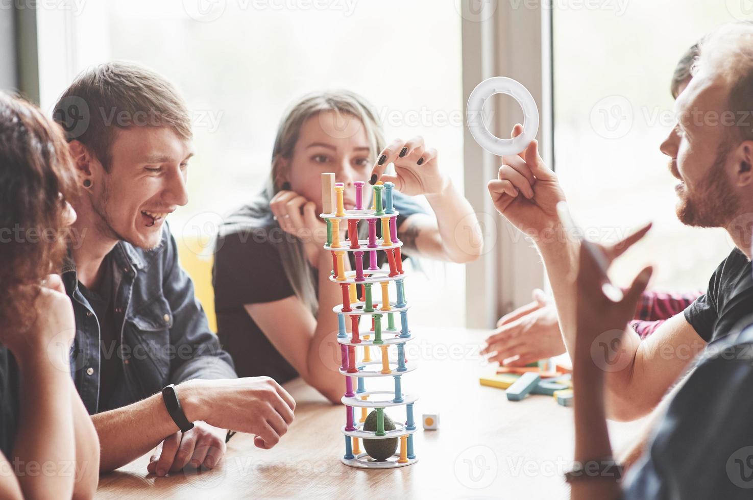 A group of creative friends sitting on a wooden table. People were having fun while playing a board game. photo