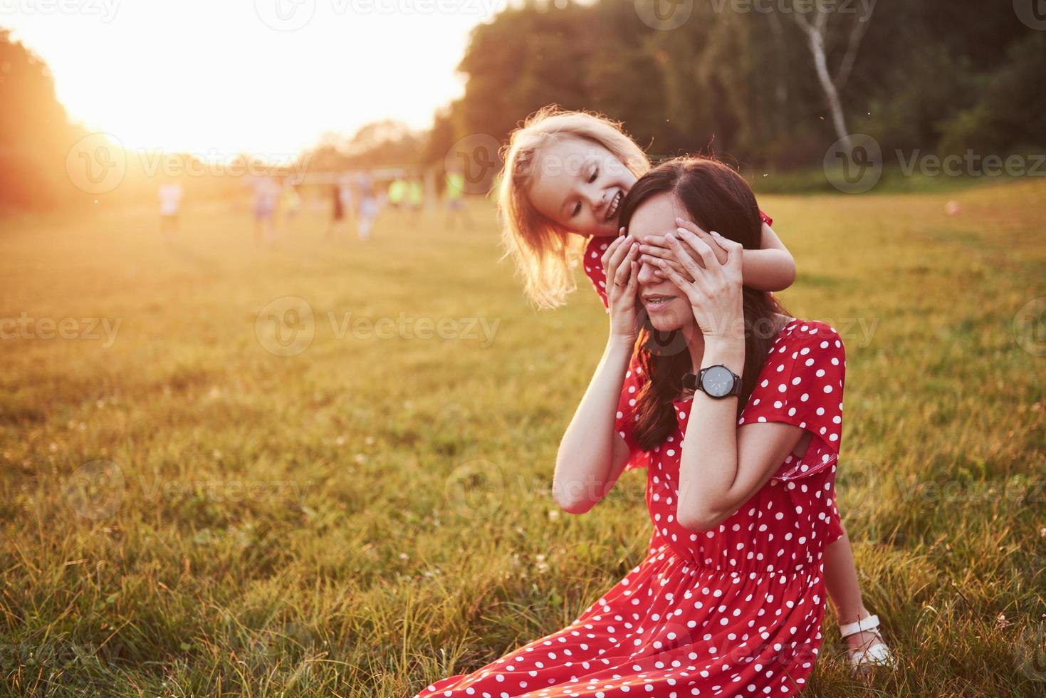 Mother plays with her daughter on the street in the park at sunset photo