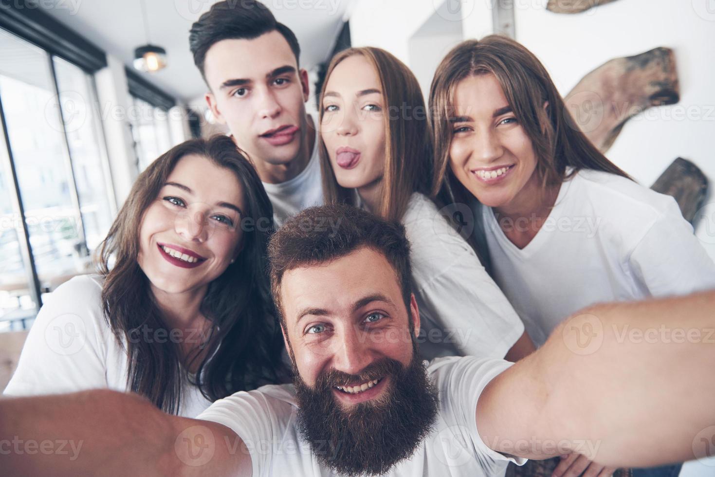 A group of people make a selfie photo in a cafe. The best friends gathered together at a dinner table eating pizza and singing various drinks