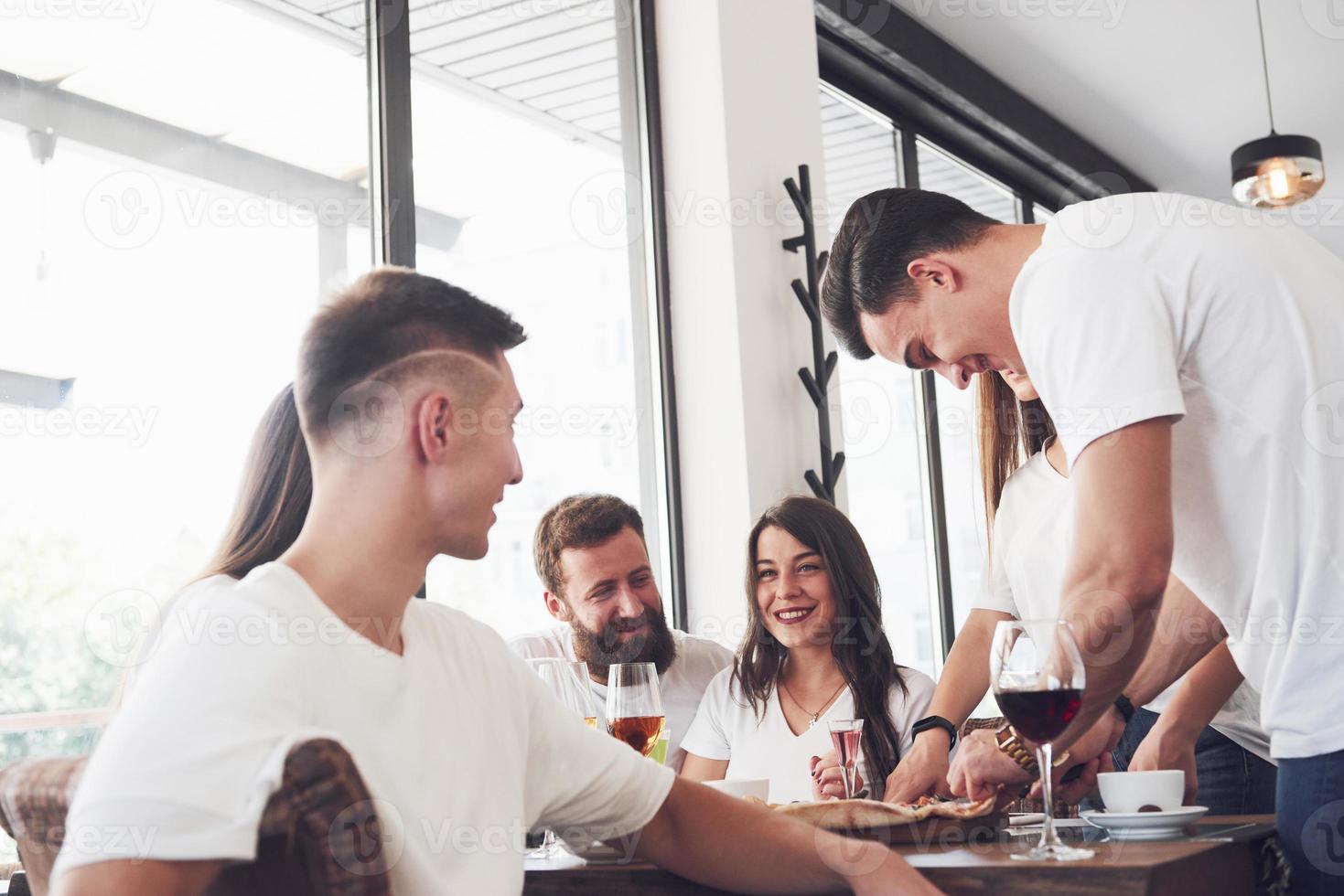 Sabrosa pizza en la mesa, con un grupo de jóvenes sonrientes descansando en el pub foto