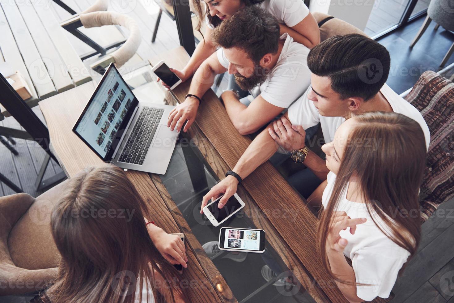A group of young people with gadgets and a laptop arrange a brainstorm and communicate with each other. The concept of developing a young business photo