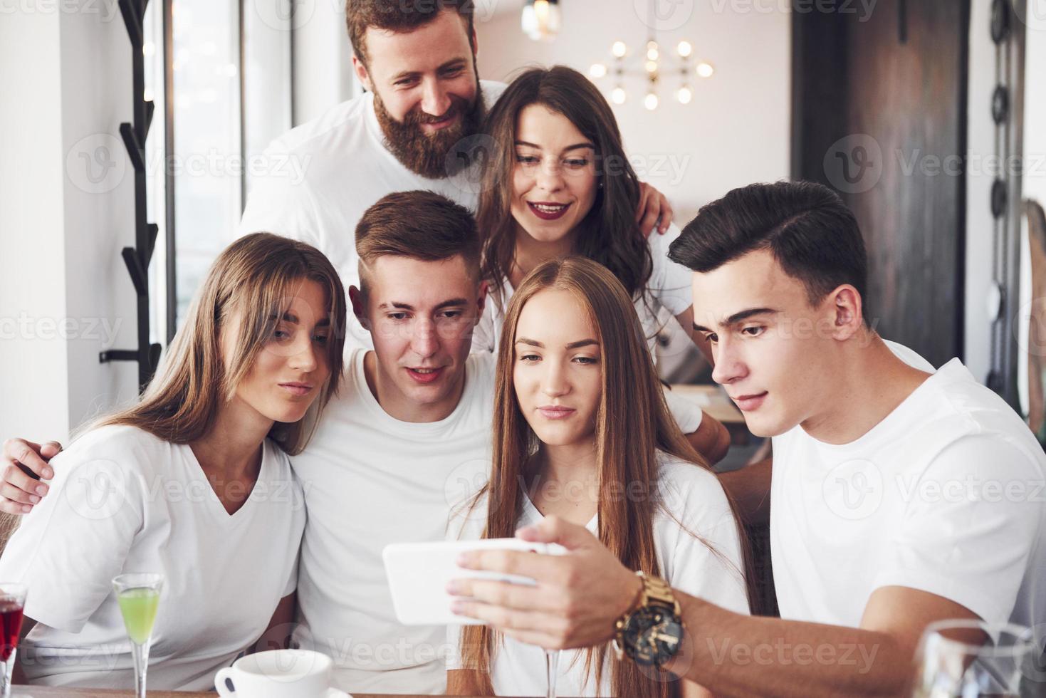 A group of people make a selfie photo in a cafe. The best friends gathered together at a dinner table eating pizza and singing various drinks