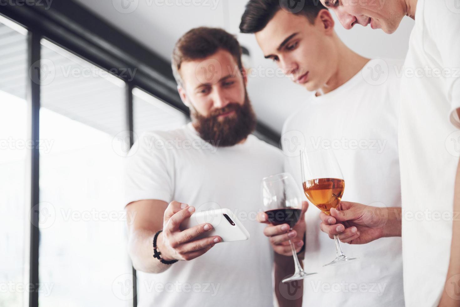 Cheerful old friends communicate with each other and phone watch, with glasses of whiskey or wine in pub. Concept of entertainment and lifestyle. Wifi connected people in bar table meeting photo