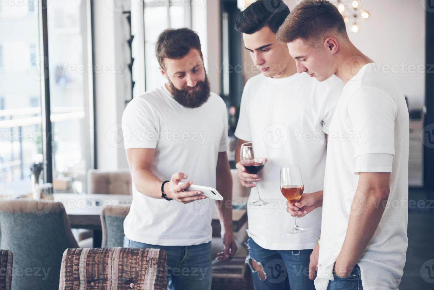 Cheerful old friends communicate with each other and phone watch, with glasses of whiskey or wine in pub. Concept of entertainment and lifestyle. Wifi connected people in bar table meeting photo