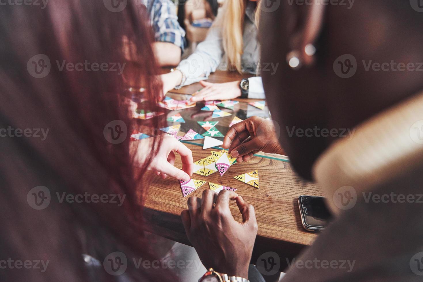 Group of creative multietnic friends sitting at wooden table. People having fun while playing board game photo