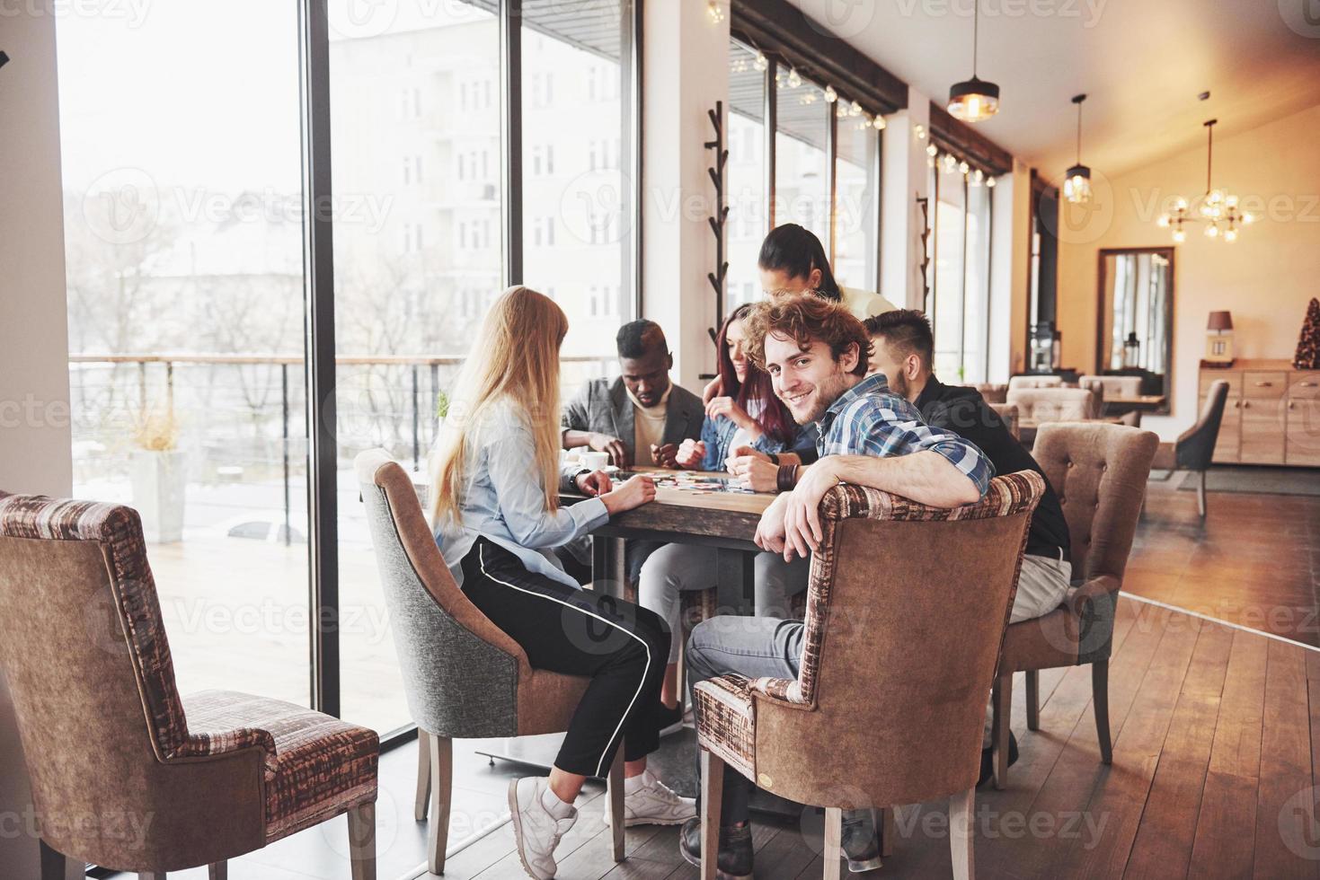 Group of creative multietnic friends sitting at wooden table. People having fun while playing board game photo