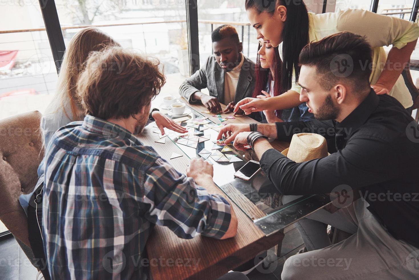 grupo de amigos creativos sentados en la mesa de madera. gente divirtiéndose mientras juega al juego de mesa. foto