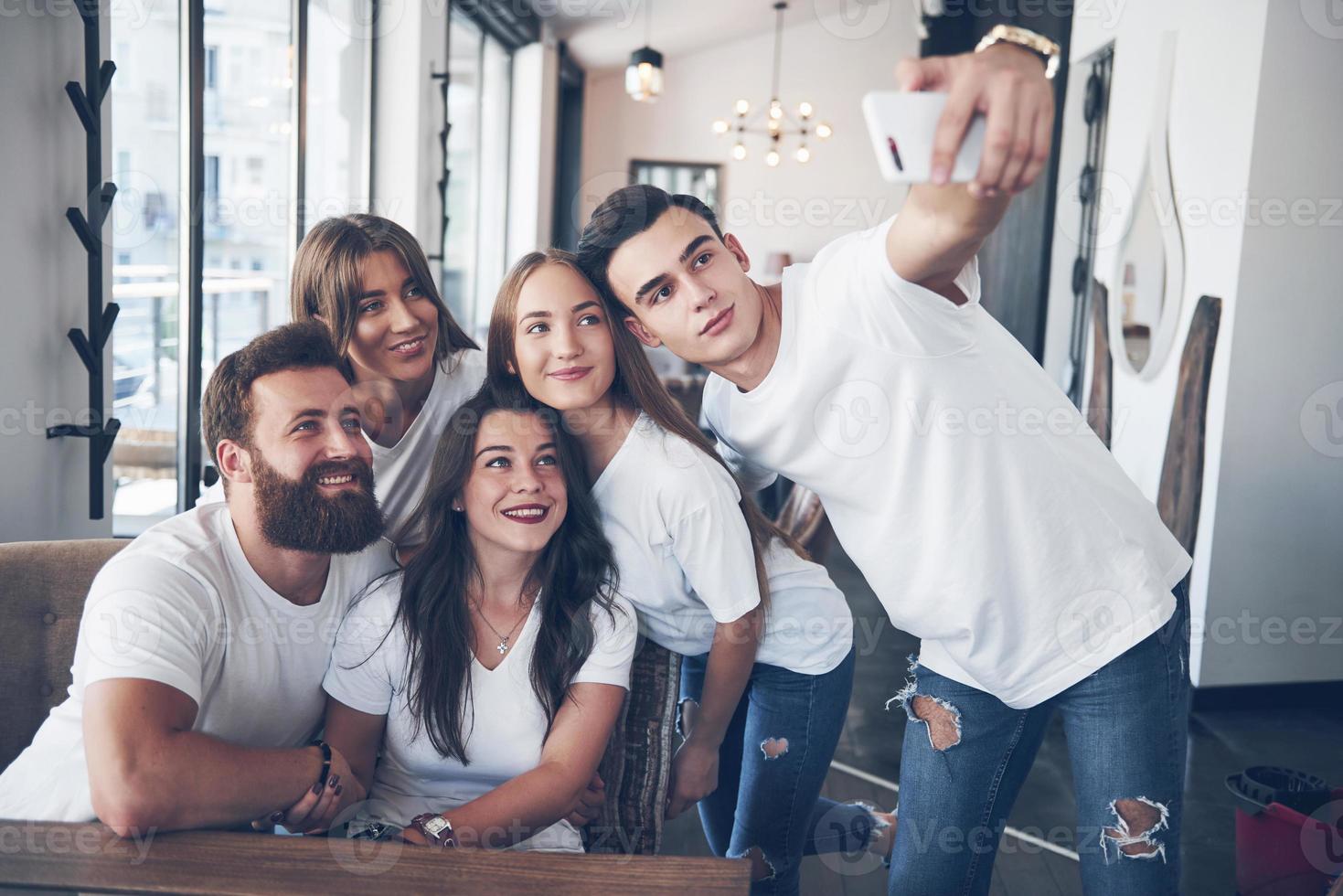 A group of people make a selfie photo in a cafe. The best friends gathered together at a dinner table eating pizza and singing various drinks