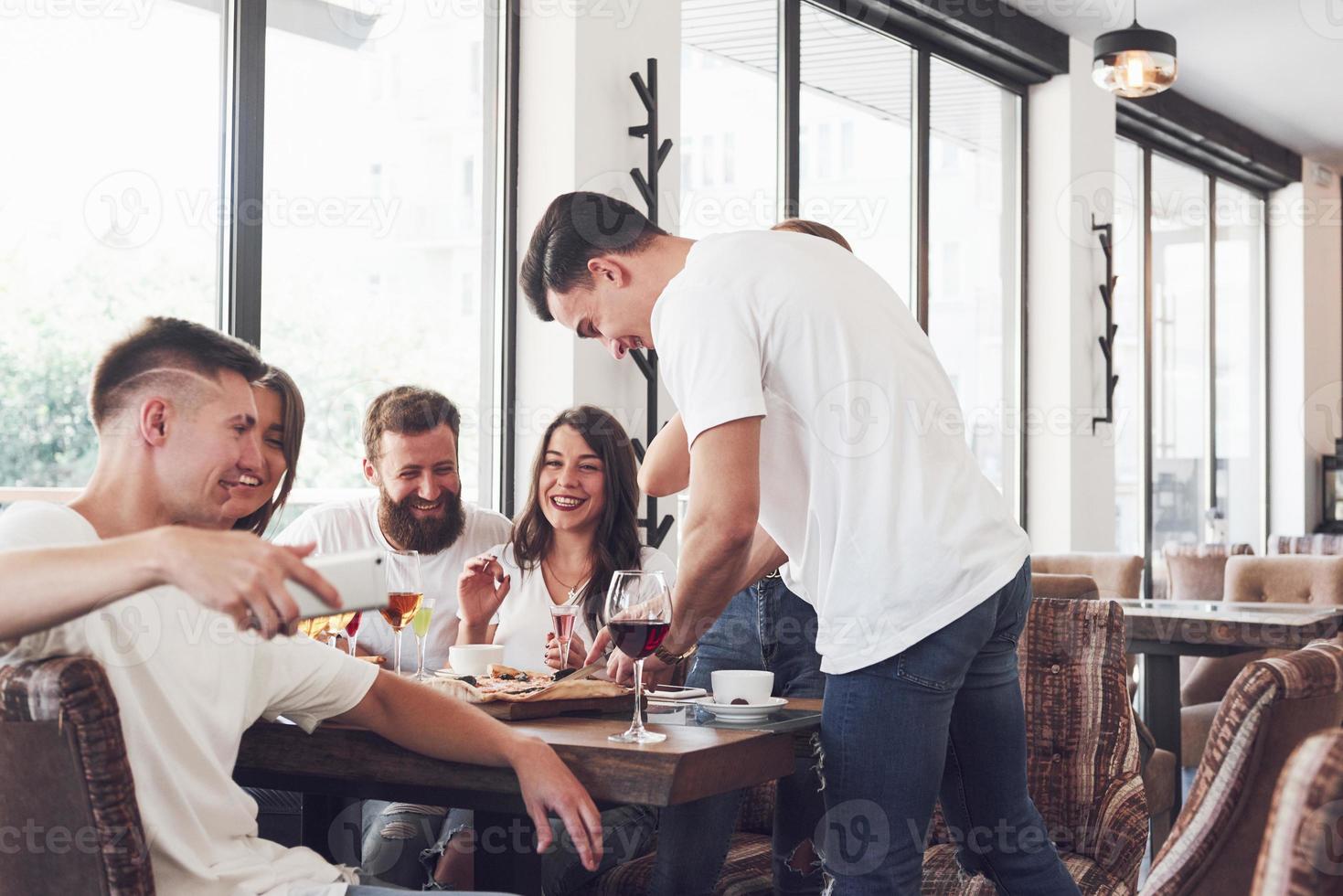 Tasty pizza on the table, with a group of young smiling people resting in the pub photo